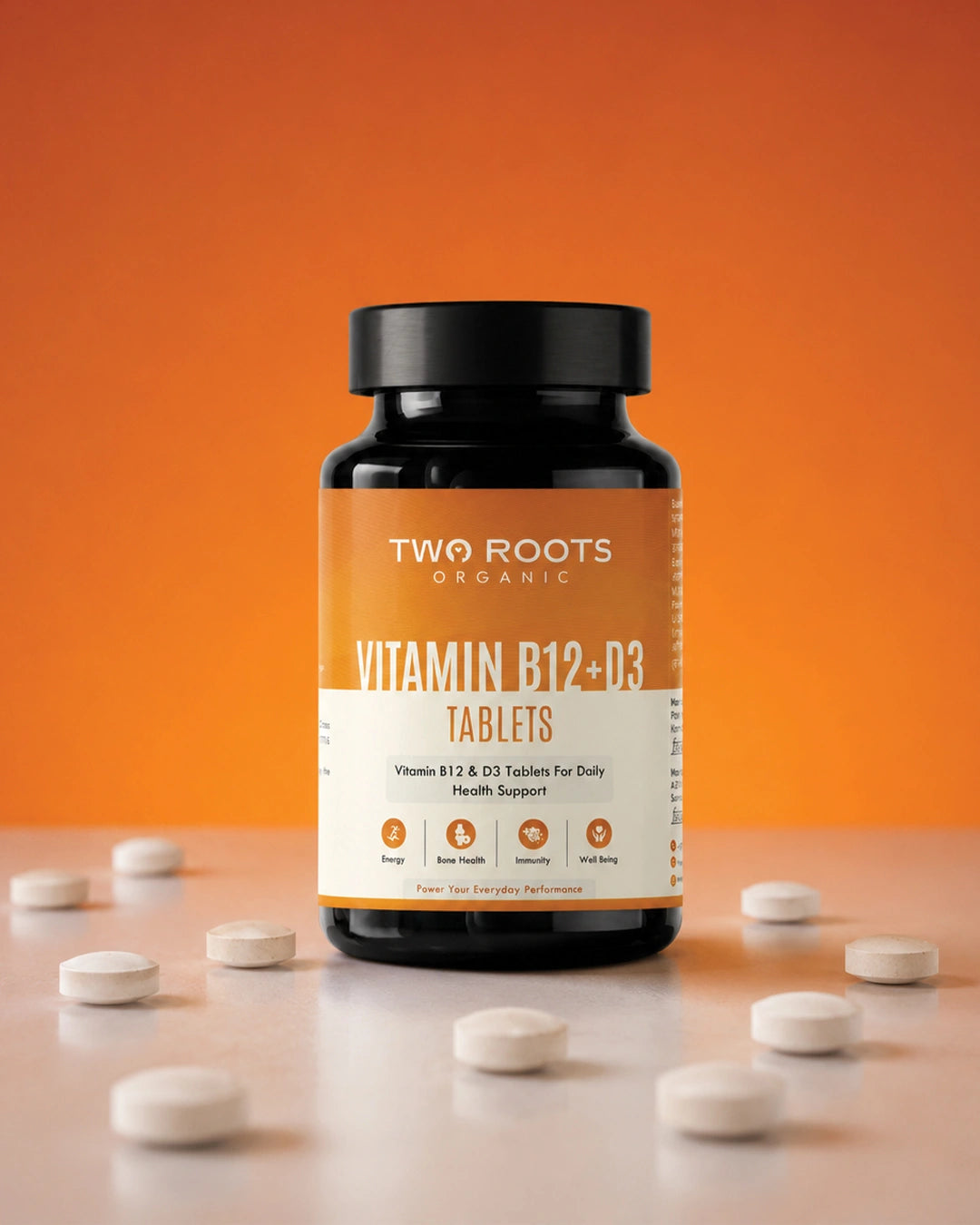 Bottle of Two Roots Organic Vitamin B12+D3 Tablets on an orange background with scattered tablets.